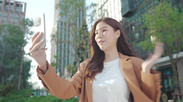 Asian Business Smiling woman video calling outdoors in city while enjoying her smartphone experience. Remote work Technology. Communication with temwork. happiness in outdoor city. influencer work