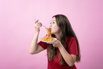 Young woman in a red shirt with long brown hair holds a fork and plate of noodles, shouting excitedly. The scene has a pink background, creating a lively and humorous atmosphere.