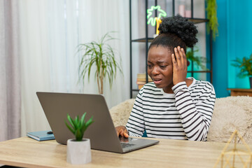 African American woman reading email on laptop at home. Stressful expression, bad news received,...