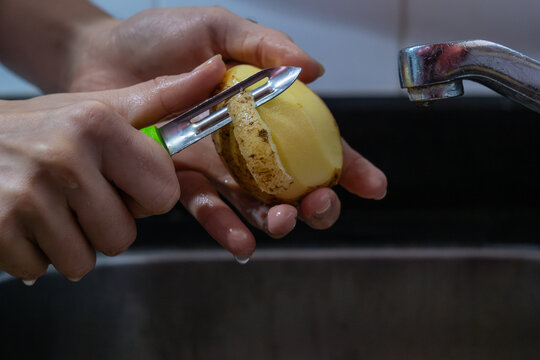 Potapo peeling. Hands peeling raw potato with vegetable peeler in the kitchen.