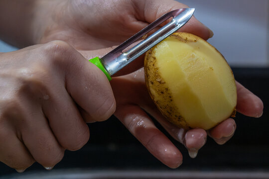 Potapo peeling. Hands peeling raw potato with vegetable peeler in the kitchen.