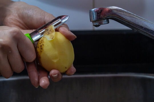 Potapo peeling. Hands peeling raw potato with vegetable peeler in the kitchen.