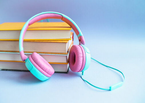 Stack of books and headphones on a purple background. Audiobook concept. Listen to lessons.