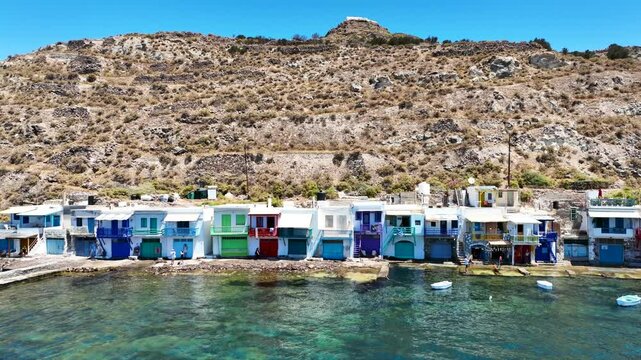 Aerial drone cinematic video of iconic and picturesque fishing village of Klima built by the shore with colourful traditional fishing boat houses called syrmata in island of Milos, Cyclades, Greece