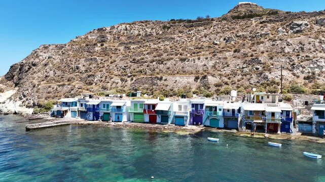 Aerial drone cinematic video of iconic and picturesque fishing village of Klima built by the shore with colourful traditional fishing boat houses called syrmata in island of Milos, Cyclades, Greece