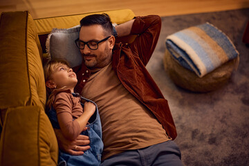 Fototapeta premium Above view of smiling father and daughter relaxing on sofa.