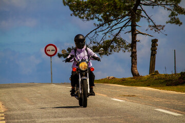 Obraz premium Primer plano de una chica motociclista avanzando por una carretera rural con un cartel de prohibido adelantar al fondo.