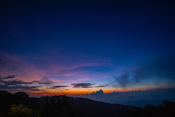 stunning mountainous landscape at sunrise with vibrant orange and pink hues illuminating the clouds against a blue sky. layer of mist settled in the valley, giving the scene a dreamy.
