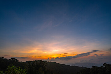 Fototapeta premium stunning mountainous landscape at sunrise with vibrant orange and pink hues illuminating the clouds against a blue sky. layer of mist settled in the valley, giving the scene a dreamy.