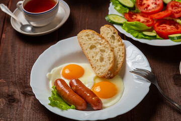 Breakfast two plates fried eggs with sausages white bread and tea in cups on a wooden table