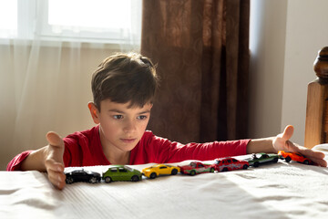 A young boy, aged 6-8, plays with toy cars in a sunny, cozy room, aligning them in a row. The scene...