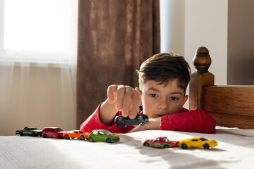 A young boy, aged 6-8, plays with toy cars in a sunny, cozy room, aligning them in a row. The scene highlights themes of autism, developmental disorders, childhood play, and mental well-being.