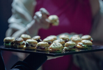 view of a bunch of mini burgers on a plate held by a server at an event indoor
