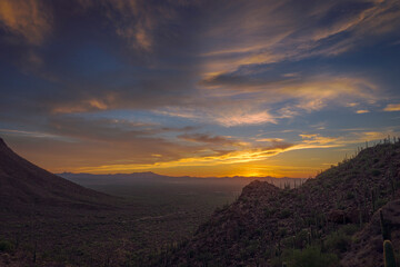 A breathtaking sunset sky over a tranquil desert scene with cacti and rugged mountains. Warm and vivid colors blend harmoniously, creating a calm and serene atmosphere showcasing the beauty of nature.