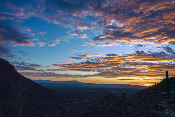 Sunset creating vibrant cloud formations over a desert landscape, showcasing natural beauty and tranquility. Captured with hills, cacti, and expansive horizons, providing a stunning and peaceful view.
