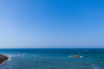 Naklejka premium vast expanse of blue ocean meeting a clear blue sky, punctuated by a small rocky island and a few swimmers in the distance, creating a minimalist and calming composition