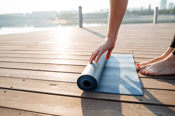 A woman is gently rolling up a vibrant yoga mat on a beautiful sunlit wooden deck, capturing the...