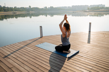 A woman is peacefully sitting on a yoga mat positioned on a beautiful dock that overlooks a serene...