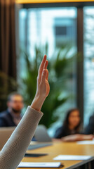 Photo Description: An office worker raising their hand to speak during a meeting