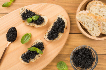 Bread slice with black caviar served on on wooden background, top view