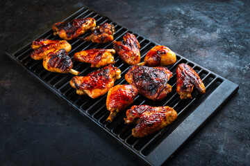 Traditional barbecue chicken wings, drumsticks and chicken breast with hot chili sauce served as close-up on a rustic grill grate