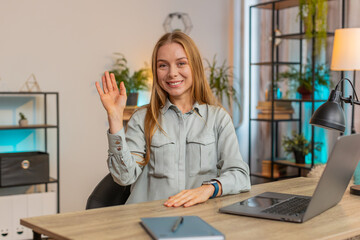 Hello. Happy mature Caucasian businesswoman waves hand hi gesture greeting welcomes someone, online webinar, remote distance conversation. Freelance girl with laptop sitting at desk looking at camera. © Andrii Iemelianenko