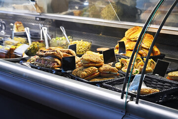 Display case of a deli or bakery. There are various types of sandwiches, pastries, and other prepared foods.