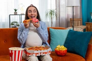 Pregnant woman eating unhealthy junk food pizza, popcorn crisp sitting on sofa watching TV movie in...