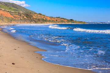 A beautiful beach with a blue ocean and a rocky cliff in the background