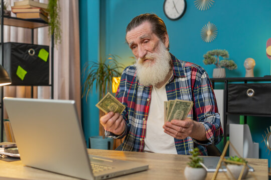 Caucasian elderly man freelancer counting cash insufficient amount of money. Financial crisis. Bankruptcy. Poverty and destitution. Sad upset grandpa with laptop netbook sitting at home office table.