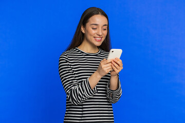 Caucasian woman texting share sms messages content on smartphone social media applications online, watching relax movie browsing. Young girl uses mobile phone smile isolated on blue background indoors