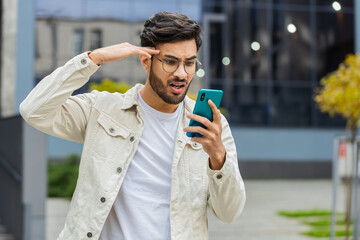 Surprised Indian man use smartphone typing browsing, loses becoming surprised sudden lottery...