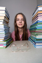 Student Sitting Between Stacks of Books. A young girl sitting between two tall stacks of books on a...