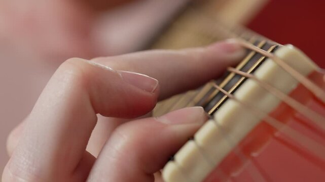 Extreme close-up of woman's fingers strumming chord on fretboard of six string acoustic guitar is absolutely thrilling to watch. Guitarist's passion for mastering craft is evident as practices daily