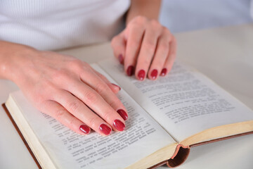 Woman with red nail polish holding a book while reading. Education and manicure concept. Close-up.