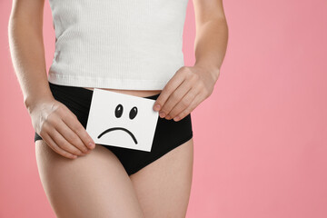 STD (sexually transmitted disease). Woman holding sticky note with drawn sad face on pink background, closeup. Space for text