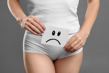 STD (sexually transmitted disease). Woman holding sticky note with drawn sad face on grey...