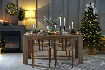 Christmas table setting with stylish dishware, glasses and burning candles in festive decorated room
