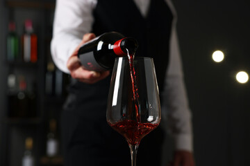 Professional sommelier pouring red wine into glass indoors, closeup