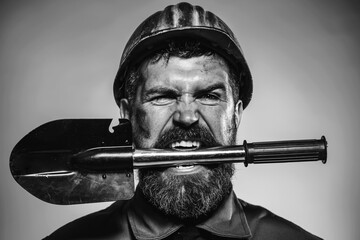 Male builder or miner in protective helmet with shovel in teeth. Mining, heavy industry,...