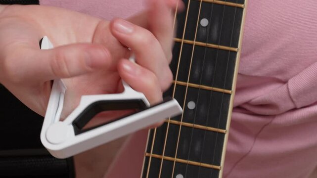 Extreme close-up woman's fingers attaches capodastro to classical guitar. Strap-on capo includes semi flexible plastic strap connected to bar on one side and adjustable on other side by ratchet system