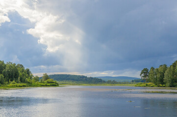 Dark clouds before thunderstorm with ray of light on lake. Dramatic sky.