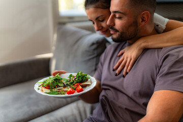 Woman shares tender moment with her partner, delivering homemade breakfast and a loving kiss in cozy living room.