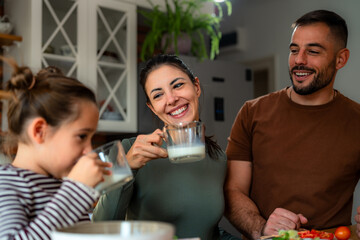 In a relaxed atmosphere, the parents and child have fun drinking milk as they together prepare a nutritious breakfast in the comfortable environment of their dwelling.po