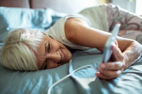 Senior woman using smartphone in bed - Powered by Adobe