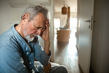 Senior man sitting in pajamas with headache in bedroom