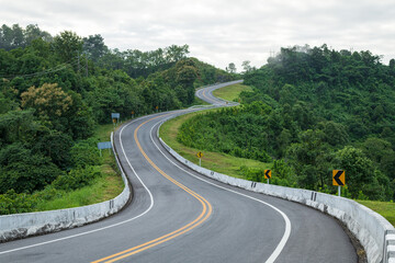 Long curvy forest asphalt road over the hills. Beautiful curved road in the forest. Side view of road