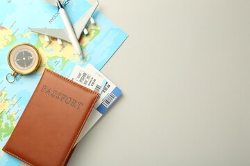 Passport with tickets, plane model, map and compass on light background, flat lay. Space for text