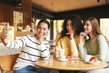 Happy friends taking selfie during coffee meeting in cafe