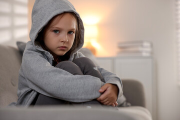 Orphanage concept. Sad girl sitting on sofa indoors